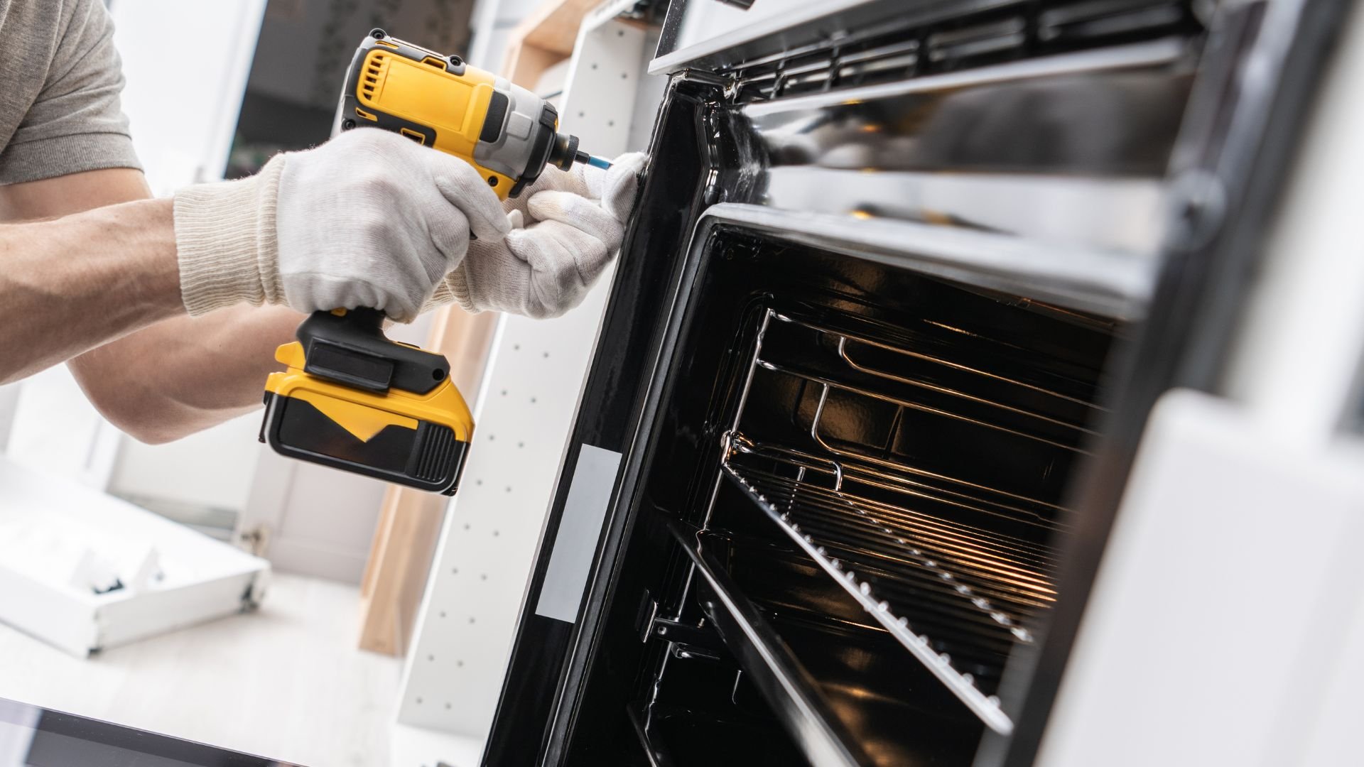 Technician using yellow drill to repair or install kitchen oven appliance